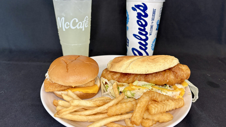 McDonald's and Culver's fish sandwich meals with fries on a white plate with two drinks in the background
