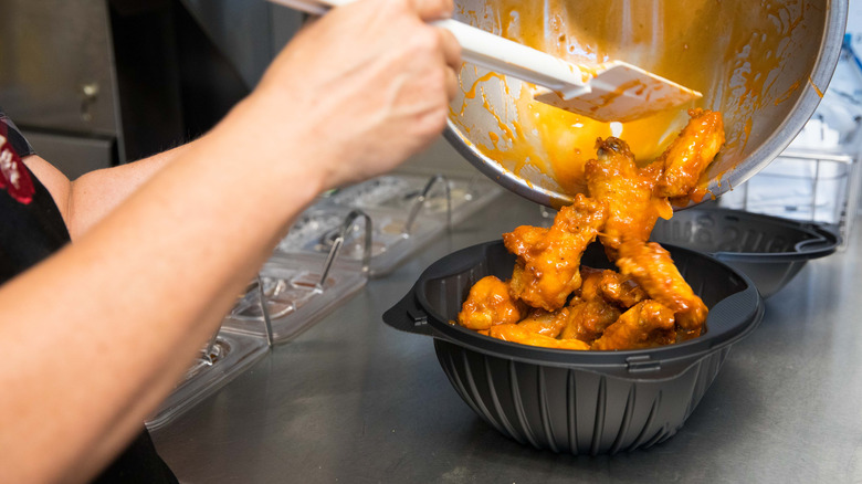 Person adds freshly prepared Buffalo wings into Pizza Hut takeout carton.