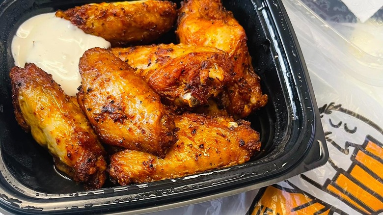 Little Caesars chicken wings in a black takeout container with sauce.