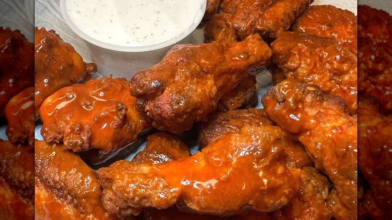 Jet's Pizza chicken wings drenched in Buffalo sauce next to ranch dressing.