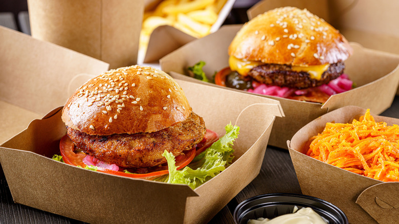 Chicken sandwich, hamburger, and other fast food items in takeout containers.