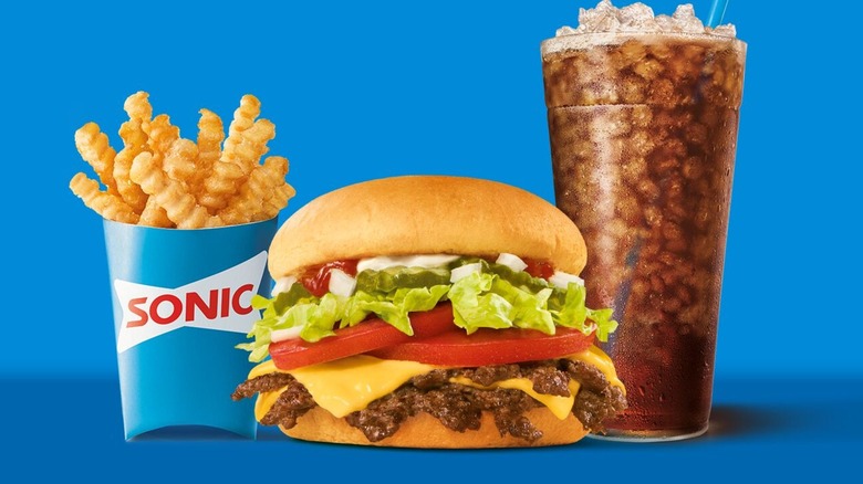 Sonic All-American Smasher between beverage and carton of fries on blue background.