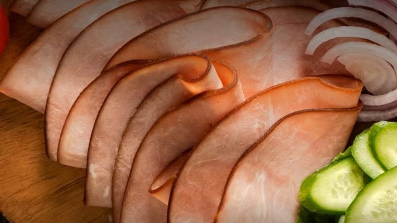 Folded slices of Black Forest ham on a cutting board with other foods.