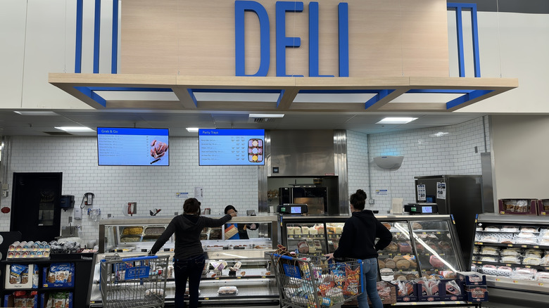 Customers with shopping carts standing at Walmart's deli counter.