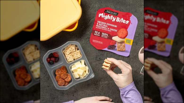 Person eating a snack pack with pepperoni, cheese, crackers, and fruit snacks.