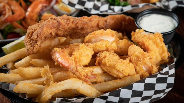A basket of fried shrimp and fish with other types of seafood in the background.