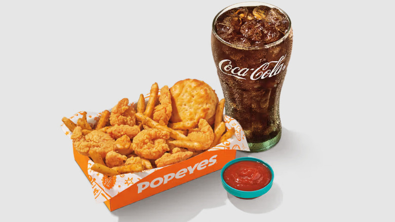 A fast food meal with shrimp, fries, and a biscuit next to a glass of soda.