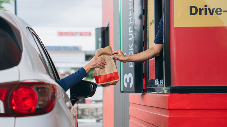 Customer in car taking to-go bag from worker in fast food drive-thru.