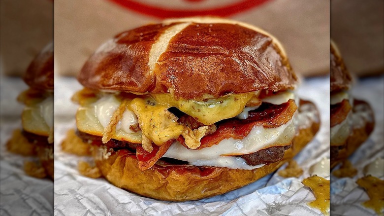 Loaded pub burger on pretzel bun with pickles, sauces, fried onions, bacon, and cheese.