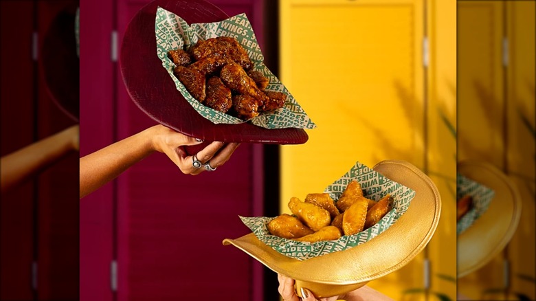 Two cowboy hats containing barbecue chicken wings held aloft by two people.