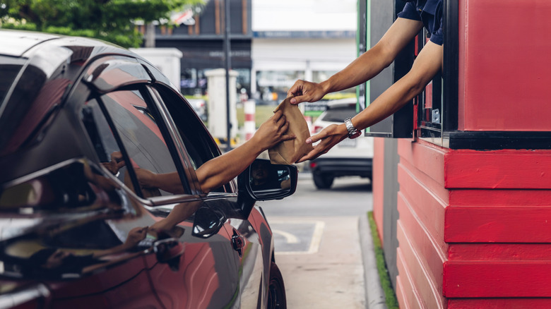Fast food drive-thru customer in car receiving a bag of food from an employee.