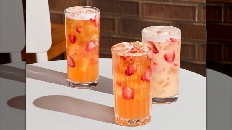 Three versions of Starbucks' mango strawberry Refresher beverages on white table.