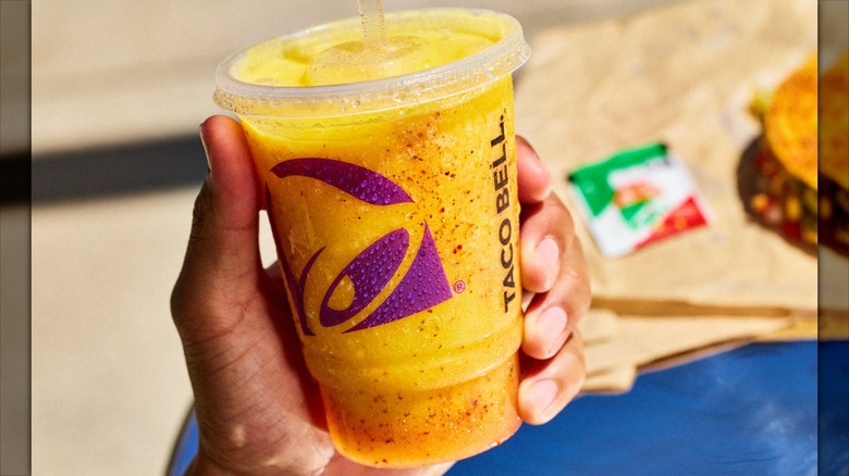 Person holding frozen pineapple beverage in branded Taco Bell cup.