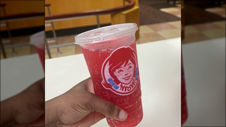 Person holding pink soda beverage in branded Wendy's cup.
