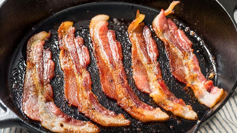 Five cooked bacon strips in cast iron skillet.