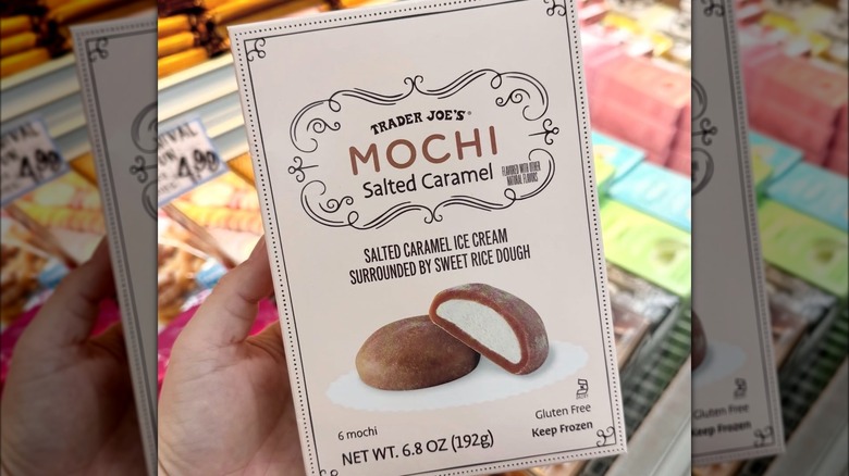 A hand holds up a beige box labeled "Trader Joe's Mochi Salted Caramel" with a picture of the mochi.
