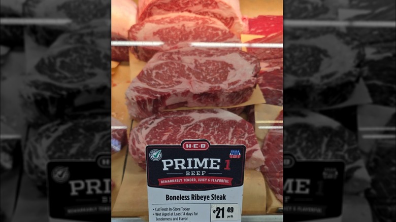 A row of USDA Prime ribeye steaks displayed behind a glass case at an H-E-B supermarket
