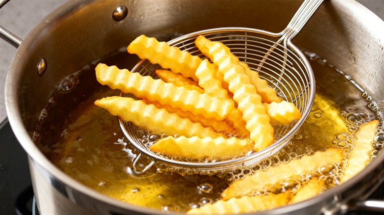 Crinkle-cut fries getting cooked a second time in oil for extra crispiness.