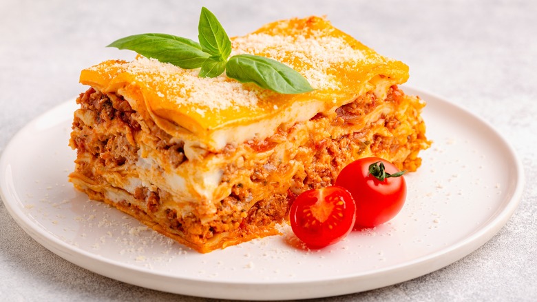 Lasagna on white plate topped with fresh basil 