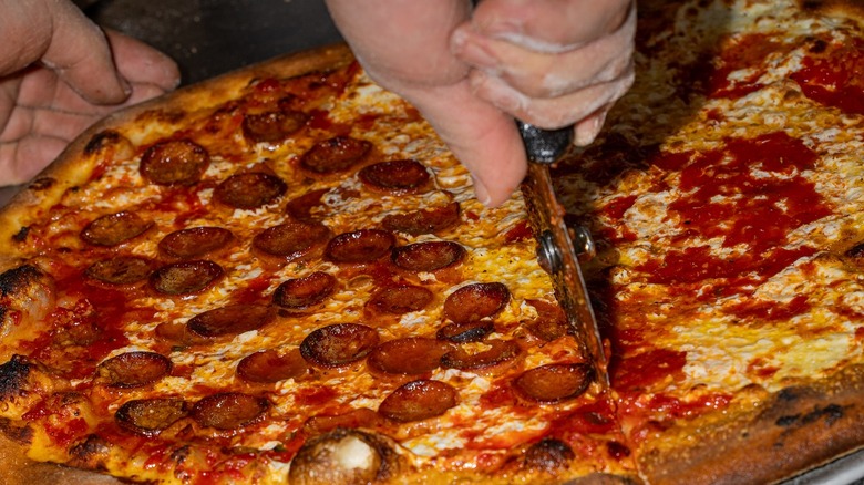 Hand slicing pizza that's half pepperoni, half cheese