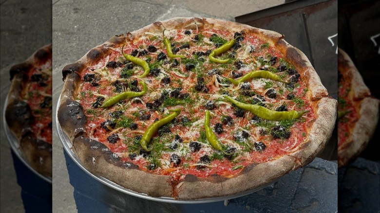 Fresh pizza topped with olives, peppers, and herbs