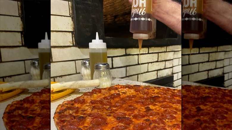 Honey being drizzled on a large pepperoni pizza