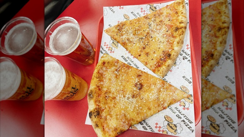 Two slices of cheese pizza on a plastic tray next to two beers