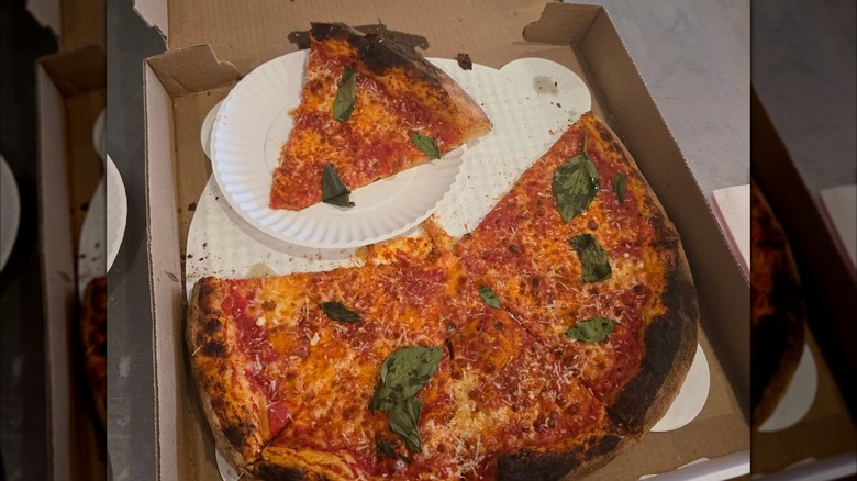 An open pizza box with a partially eaten cheese pizza topped with basil