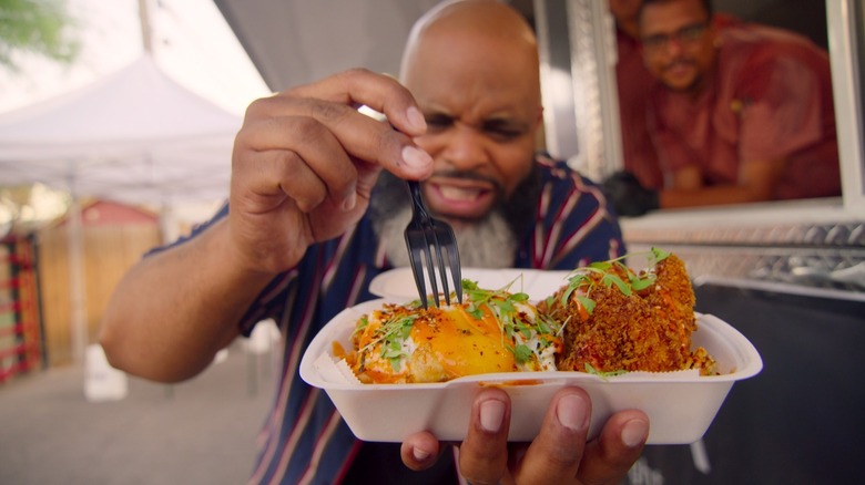 Daym holds a fork and a takeout meal