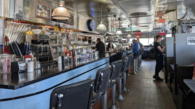 The interior of the Deluxe Town Diner in Massachusetts with a row of bar seating and chrome walls