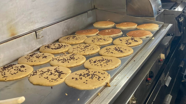 Multiple chocolate chip pancakes on a flat-top grill at Deluxe Town Diner