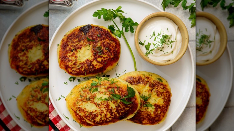 Meat and potato patties garnished with fresh herbs served with a side of sour cream