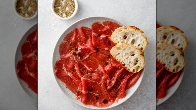 Thinly-sliced beef with toasted baguette on top next to a bowl of spices