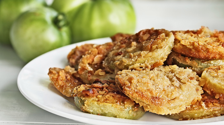 A plate of fried tomatoes with fresh tomatoes in the background