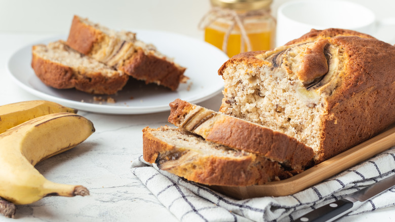 Banana bread on a cutting board with two slices stacked on a plate in the background