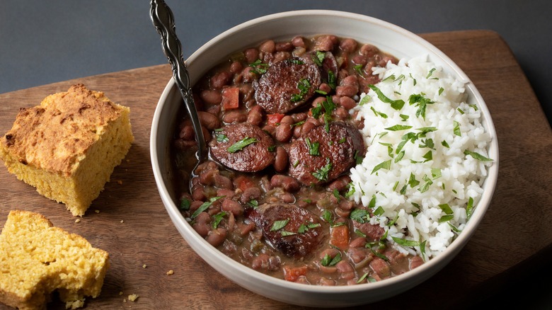 A bowl of red beans and rice with sausage on a wooden cutting board with cornbread