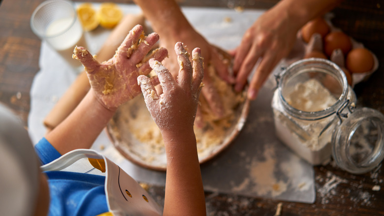 Child's hands covered in dough with adult hands in background kneading dessert dough