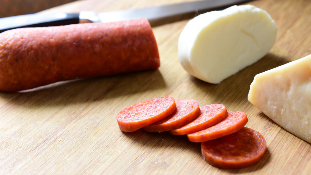 Pepperoni with slices on board with knife and cheeses