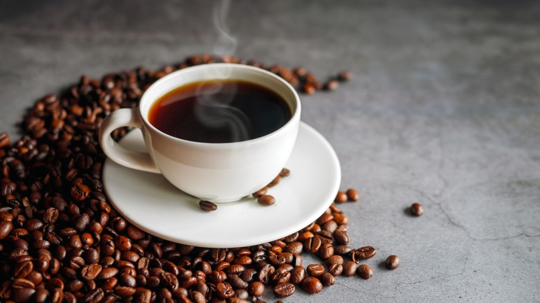 steaming cup of coffee surrounded by coffee beans