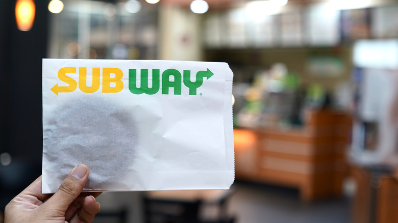 A subway cookie in a wrapper being held up in a Subway restaurant