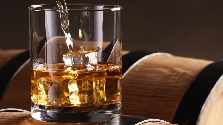 Whiskey poured into a glass with ice on top of barrels