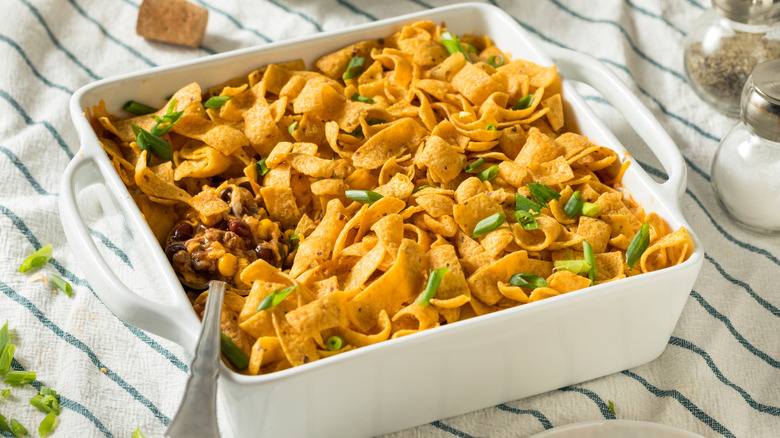 White casserole dish of Frito pie on white and blue striped blanket.