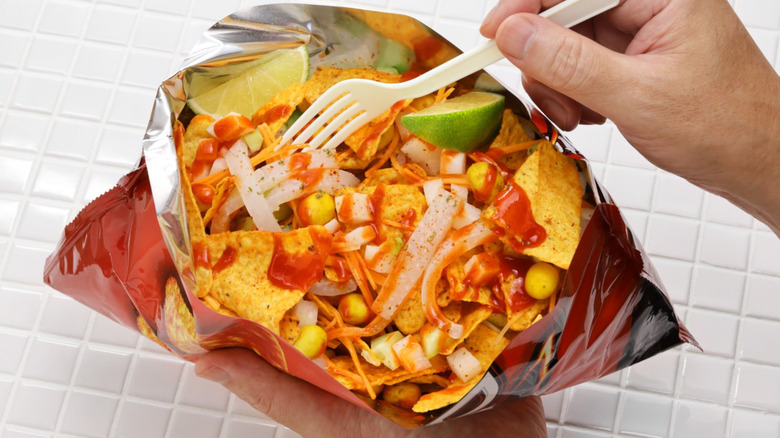 Hands holding walking taco in Doritos bag over white tile.