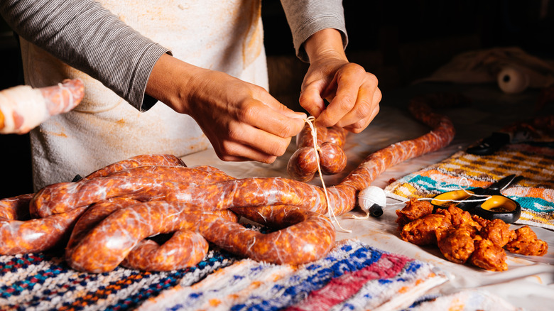 Closeup of person making handmade pork sausages with string and natural casing