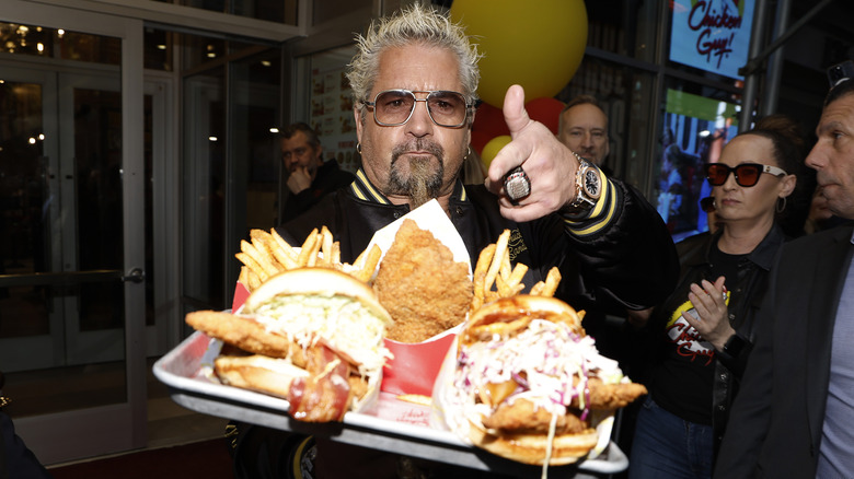 Guy Fieri with a tray of burgers, fries, and fried chicken