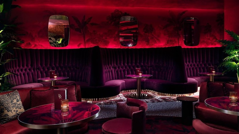 Red lighted room with velvet booths and round tables