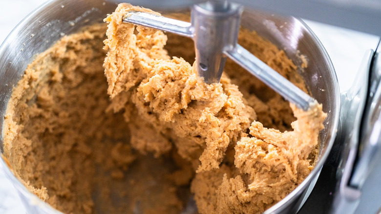 Stand mixer with cookie dough batter around metal bowl and on paddle attachment