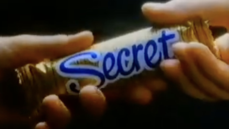 A hand holding a Nestlé Secret candy bar in gold wrapper with blue logo