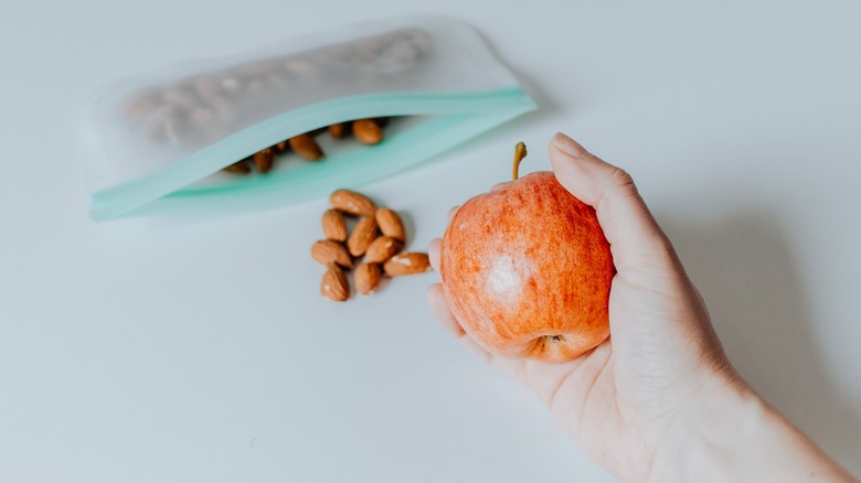 Hand holding apple next to almonds in Ziploc bag
