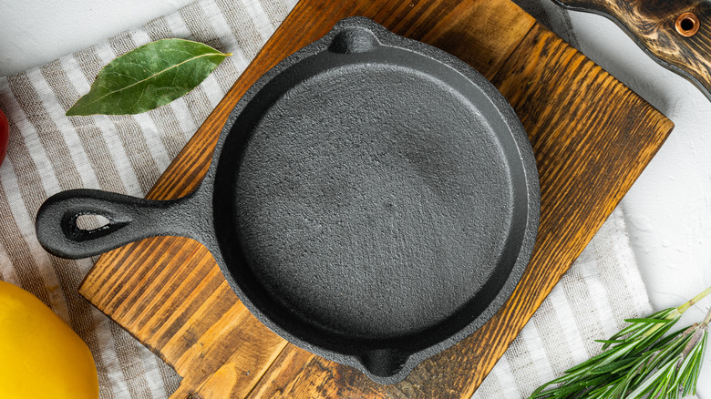 A cast iron skillet on a cutting board on a striped cloth with herbs nearby.